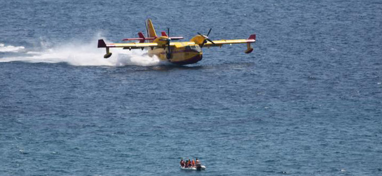 Platz da! Im Vordergrund ein Dingi mit Urlaubern und wenige Meter dahinter gleitet ein Löschflugzeug mit 150 km/H über die Wasseroberfläche. Der Flieger nimmt 5,4 Tonnen Wasser auf, bevor er wieder ins Landesinnere zum Löscheinsatz durchstartet.